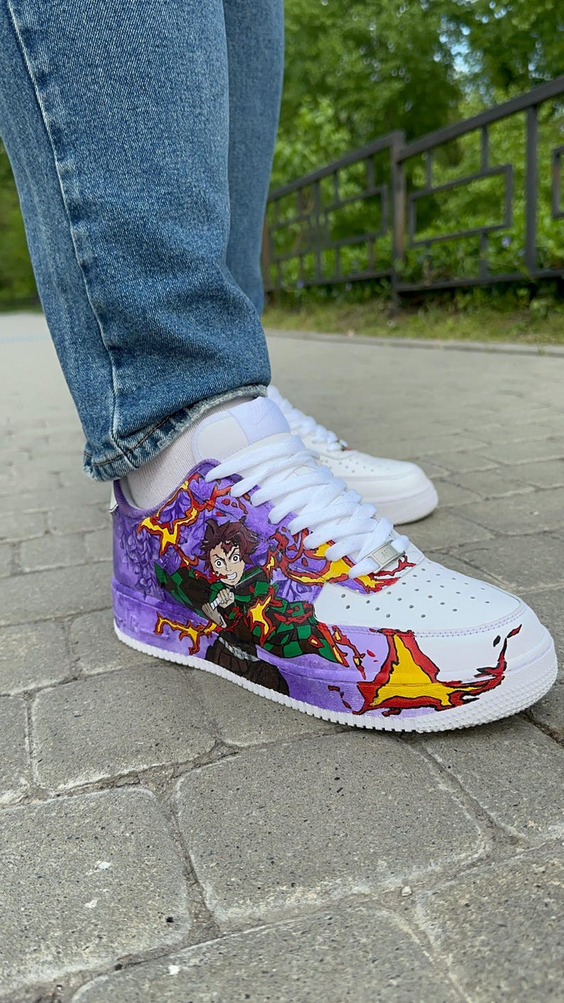 May include: White sneakers with custom artwork featuring a character in a green and black outfit with purple and yellow flames. The shoes have white laces and a purple and white design on the sides.