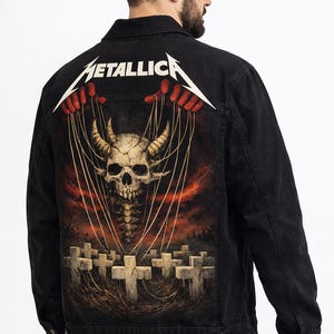 Può includere: Giacca di jeans nera con grafica di teschio e cimitero sul retro, e la scritta "METALLICA" in bianco. La giacca ha una chiusura con bottoni e due tasche sul petto. Il design ricorda l'artwork di un album di una band heavy metal.
