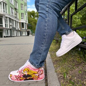 May include: White sneakers with custom artwork. One shoe features a pink and red design with a character illustration and yellow hair. The other shoe is plain white. The person is wearing blue jeans.