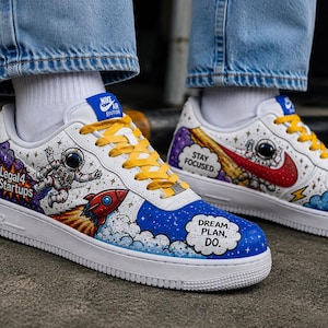 May include: White sneakers with yellow laces featuring custom space-themed artwork including an astronaut, a rocket, and clouds. The text "Legal4 Startups" appears on the side, while "STAY FOCUSED" and "DREAM. PLAN. DO." are printed in speech bubbles.