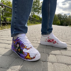 May include: White sneakers with custom artwork. One shoe features a colorful anime-style design with purple, yellow, and green accents. The other shoe has pink cherry blossom branches. Both shoes have white laces and soles.