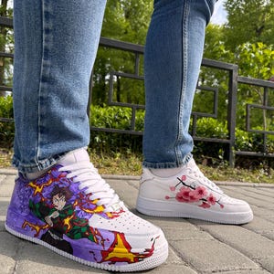 May include: White sneakers with custom artwork. One shoe features a colorful anime character design with purple, green, and yellow accents. The other shoe has a pink cherry blossom design. Both shoes have white laces and soles.
