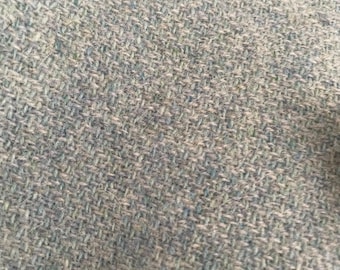 May include: Close-up of a textured fabric with a woven pattern. The fabric has a mix of light blue, gray, and white threads, creating a heathered appearance. The weave is tight, suggesting a durable material, possibly for upholstery or clothing.