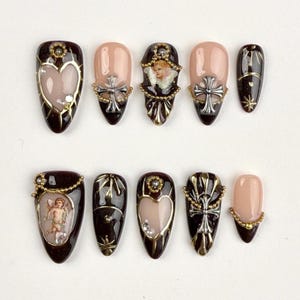 May include: A collection of ten artificial nails with diverse designs. The nails have a dark brown base with gold detailing, crosses, hearts, and angel illustrations. Some nails feature a nude base with silver and gold embellishments.