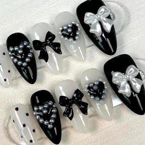 May include: Set of ten black and white nail tips with different designs. Each nail tip features a silver or white bow and a cluster of silver beads.