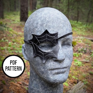 Peut inclure: Un cache-œil noir avec un motif de toile d'araignée, porté sur une tête de mannequin à la texture de pierre grise. Le cache-œil a une forme d'étoile aux bords pointus et une fine sangle noire. Un badge blanc circulaire avec le texte PDF PATTERN est visible.