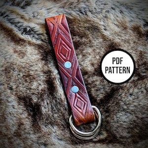 May include: A brown leather key fob with a geometric pattern and silver rivets. The fob has a silver key ring attached. The image includes the text "PDF PATTERN".