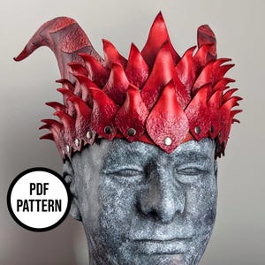 Puede incluir: Una corona de cuero rojo con un diseño en forma de llama. La corona presenta múltiples formas puntiagudas y está asegurada con remaches plateados. La corona se muestra en un busto gris con el texto "PDF PATTERN" en un círculo blanco.