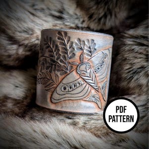 Può includere: Un braccialetto in pelle con un designo in rilievo dettagliato di una falena e fogliame. Il braccialetto è di colore marrone chiaro con un leggero bagliore. Il testo "PDF PATTERN" è visibile nell'angolo in basso a destra dell'immagine.