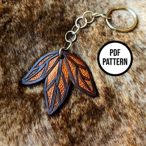 Può includere: Un portachiavi in ​​pelle con un design a foglia marrone e arancione. Il portachiavi ha un anello e una catena in metallo argentato. Il testo "PDF PATTERN" è visibile nell'immagine.