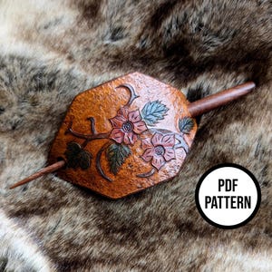 Könnte beinhalten: Ein brauner Leder-Haarstab mit geschnitzten floralen Details und einem Holzstab. Der Haarstab zeigt zwei rote Blumen, grüne Blätter und den Text "PDF PATTERN" in einem weißen Kreis.
