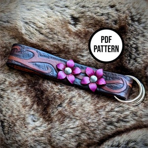 May include: A brown leather strap with a decorative floral design and two pink flowers. The strap has a metal ring attached to one end. The text "PDF PATTERN" is visible in a circle on the image.