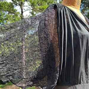 Peut inclure: Un v&ecirc;tement noir dot&eacute; de manches larges et fluides en dentelle florale complexe. Le corsage pr&eacute;sente des d&eacute;tails de tissu fronc&eacute; au niveau de l'&eacute;paule, se prolongeant par une section noire unie. Le mod&egrave;le inclut un d&eacute;collet&eacute; en V et une silhouette drap&eacute;e.