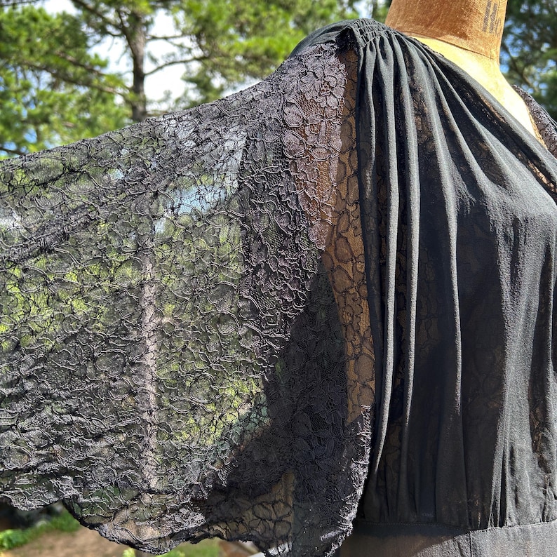 Peut inclure: Un v&ecirc;tement noir dot&eacute; de manches larges et fluides en dentelle florale complexe. Le corsage pr&eacute;sente des d&eacute;tails de tissu fronc&eacute; au niveau de l'&eacute;paule, se prolongeant par une section noire unie. Le mod&egrave;le inclut un d&eacute;collet&eacute; en V et une silhouette drap&eacute;e.