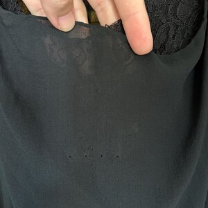Peut inclure: Un v&ecirc;tement noir compos&eacute; d'une couche de tissu transparent et l&eacute;ger sur une base en dentelle noire. La couche sup&eacute;rieure transparente pr&eacute;sente plusieurs petits trous ou accrocs distincts, r&eacute;v&eacute;lant le motif floral en dentelle dessous.