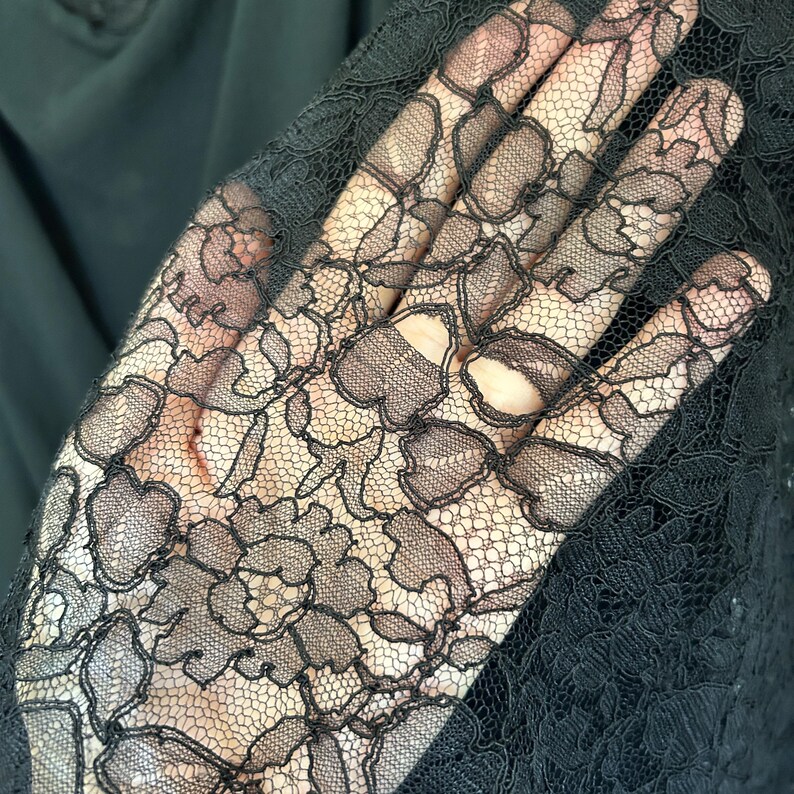 Peut inclure: Un tissu en dentelle noire transparente pr&eacute;sentant un motif floral d&eacute;taill&eacute; avec des bords festonn&eacute;s complexes et un fond en maille fine. Le textile d&eacute;licat affiche un motif botanique r&eacute;p&eacute;titif avec des p&eacute;tales et des feuilles en fil noir.