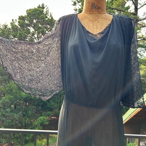 Peut inclure: Une robe bleu marine fonc&eacute; dot&eacute;e de manches &eacute;vas&eacute;es en dentelle transparente et d'un d&eacute;collet&eacute; drap&eacute;. Le corsage est confectionn&eacute; dans un tissu l&eacute;ger et semi-transparent qui se fronce &agrave; la taille, cr&eacute;ant une silhouette fluide sur un mannequin.