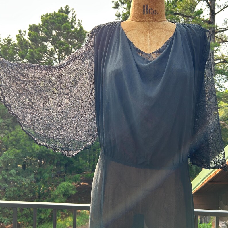 Peut inclure: Une robe bleu marine fonc&eacute; dot&eacute;e de manches &eacute;vas&eacute;es en dentelle transparente et d'un d&eacute;collet&eacute; drap&eacute;. Le corsage est confectionn&eacute; dans un tissu l&eacute;ger et semi-transparent qui se fronce &agrave; la taille, cr&eacute;ant une silhouette fluide sur un mannequin.