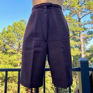 May include: Dark brown high-waisted shorts with a button closure and a tailored fit. The shorts are made of a thick, textured fabric and have a classic, knee-length design. The shorts are displayed on a mannequin.