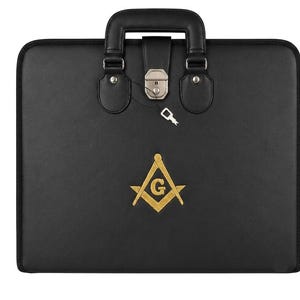 May include: A black rectangular briefcase featuring a gold embroidered Masonic square and compass emblem with a central letter G. The case includes a top handle, a silver-toned metal latch closure, and a small silver key attached by a thin cord.
