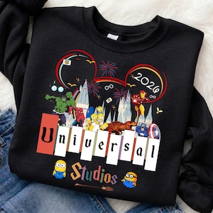 May include: Black sweatshirt featuring a colorful graphic with the text "Universal Studios" and the year "2026". The design includes cartoon characters and fireworks, with a Mickey Mouse ear outline.