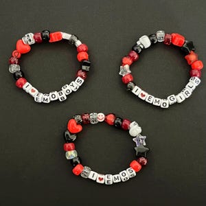 May include: Three beaded bracelets with red, black, and white beads. The bracelets spell out "I love emo boys", "I love emo girls", and "I love emos".