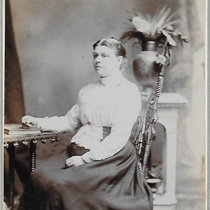Photo victorienne, Carte de cabinet, Jeune femme, Assise sur une chaise, Jupe sombre, Main sur livre, Chaise sculptée, Mode, Histoire sociale