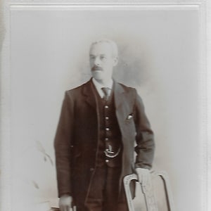 Kabinetskaart, Victoriaanse foto, Victoriaanse heer, slim pak, hand op stoel, horlogeketting, grote knoppen op vest