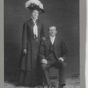 Edwardiaanse foto, dame, donkere jurk, witte veren in hoed, zittende heer, gemonteerd op kaart