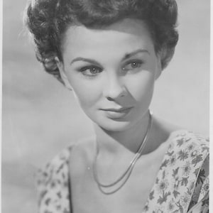 Puede incluir: Fotografía en blanco y negro de Jean Simmons, una actriz, con un vestido de estampado floral y un collar. La foto está firmada "JEAN SIMMONS."