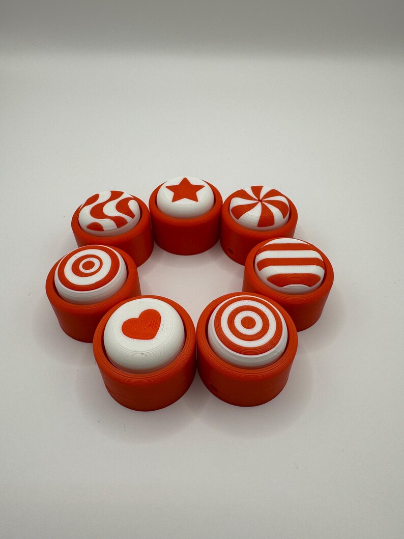 May include: Eight orange and white push buttons with different designs, including a star, heart, stripes, and swirls. The buttons are arranged in a circle.