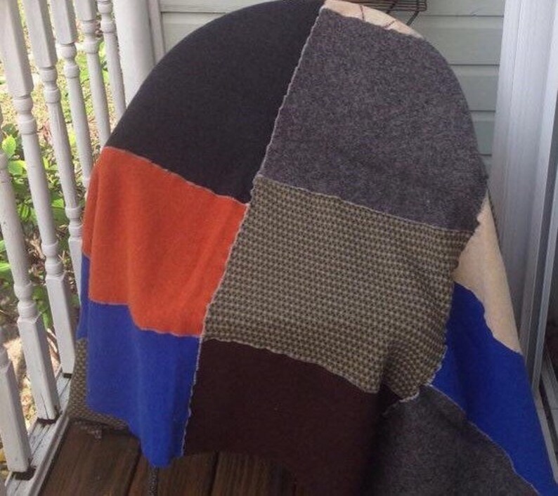 May include: A patchwork quilt made from different fabrics in shades of brown, orange, blue, and gray. The quilt is made of squares and rectangles of fabric sewn together.