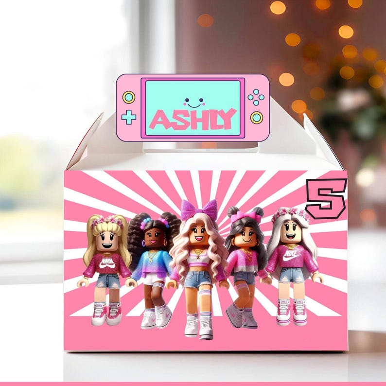 May include: Pink and white favor box with a pink and white striped background. The box has a pink and white game controller with the text 'ASHLY' on the screen. The box also has a pink and white number 5 on the side. The box features five Roblox characters in front of the game controller. The characters are all female and are wearing different outfits. The characters are all smiling and have pink hair.