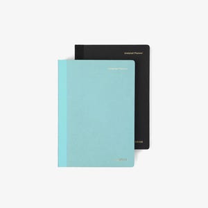 Puede incluir: Dos planificadores sin fecha, uno en color verde azulado claro y el otro en negro. El planificador verde azulado tiene un lomo azul claro y letras doradas que dicen "Undated Planner" y "grids". El planificador negro tiene letras doradas que dicen "Undated Planner".