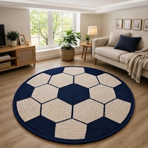 May include: A circular rug featuring a classic soccer ball pattern with alternating dark navy blue and off-white hexagonal and pentagonal shapes. The rug has a textured, crocheted appearance with visible yarn loops forming the geometric design.