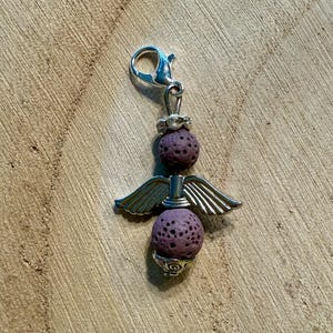 May include: A silver-toned charm with a lobster clasp, featuring two textured purple spheres and silver wings. The charm has a decorative design at the top and bottom, creating an angel-like appearance. Ideal for jewelry making.