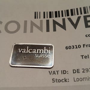 Puede incluir: Una peque&ntilde;a barra rectangular de plata con el logotipo "valcambi suisse", sobre un documento con el logotipo "COININVEST" y otro texto. La barra tiene un dise&ntilde;o geom&eacute;trico.