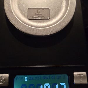 Puede incluir: Una balanza digital muestra un peso de 0,017. Una peque&ntilde;a barra rectangular plateada, etiquetada como "Irridium" y "1 gramo 99,95%", descansa sobre la superficie redonda de la balanza. La balanza es negra con varios botones.