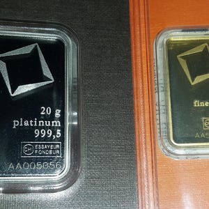 Puede incluir: Dos lingotes de metales preciosos en estuches transparentes. La barra izquierda es de platino, 20 gramos, con un dise&ntilde;o geom&eacute;trico. La barra derecha es de oro, 10 gramos, con un dise&ntilde;o similar. Ambos tienen sellos.