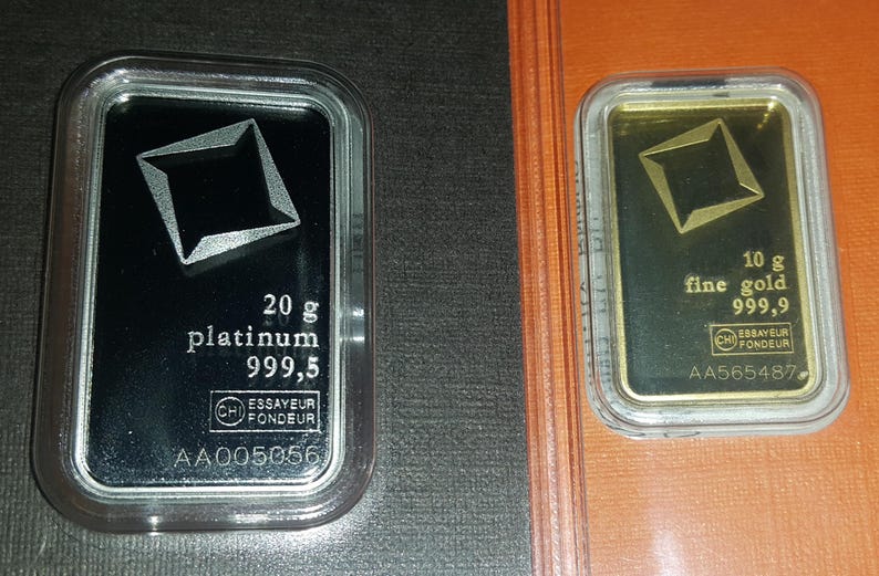Puede incluir: Dos lingotes de metales preciosos en estuches transparentes. La barra izquierda es de platino, 20 gramos, con un dise&ntilde;o geom&eacute;trico. La barra derecha es de oro, 10 gramos, con un dise&ntilde;o similar. Ambos tienen sellos.