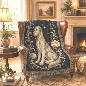 May include: A dark navy blue woven throw blanket featuring a central illustration of a light-coloured dog sitting upright. The design is framed by intricate floral scrollwork and small star motifs, finished with a decorative fringed edge.