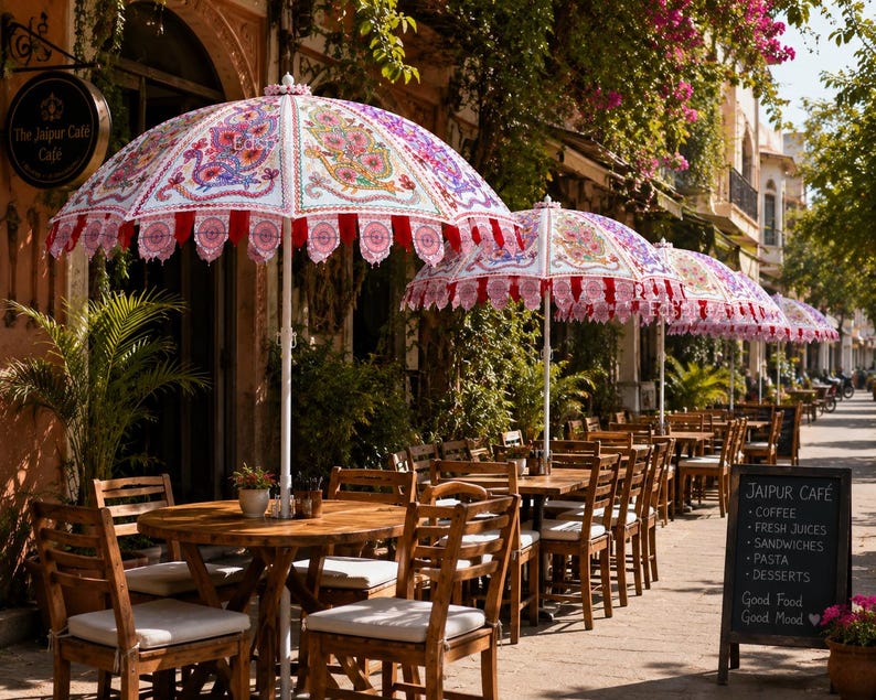 May include: A series of outdoor patio umbrellas featuring white fabric with intricate, colorful floral and bird patterns, scalloped red and white trim, and white poles, positioned over wooden tables and chairs at a sidewalk cafe.