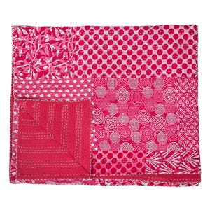 Puede incluir: Un edredón patchwork en tonos rosa y blanco. El edredón presenta varios patrones, incluyendo lunares, diseños florales y círculos concéntricos. Los bordes están acabados con un borde contrastante y costuras blancas.