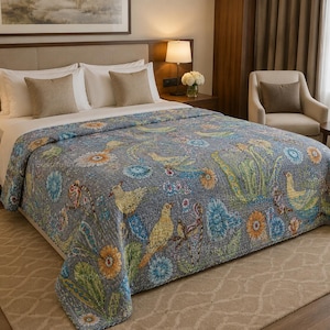 May include: A gray quilt featuring a colorful pattern of yellow birds, green foliage, and blue and orange flowers. The textile has visible stitching throughout, covering a bed with white pillows and tan accent cushions in a bedroom setting.