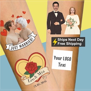 Op de afbeelding: Twee lichtgekleurde houten oppervlakken met aangepaste trouwafbeeldingen. De ene kant toont een kussend stel met rode harten en een banner met de tekst JUST MARRIED, plus een roos in een hart met de tekst Leo & Mia 21.05.2026. De andere kant toont een stel.