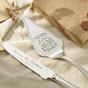 Könnte beinhalten: Silbernes Tortenheber- und Messerset mit eingravierten Details. Auf dem Messer steht "Monroe & Matthew" und das Datum "12-07-2025". Der Servierer hat ein verziertes Blumendesign. Ein Jutebeutel und Wachssiegel sind im Hintergrund.