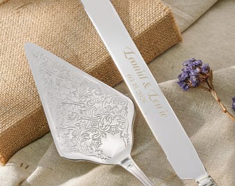 May include: A silver cake server with an intricate floral engraving and a matching silver cake knife featuring the engraved text "Leonid & Lenie" and the date "03.15.2026" on the blade, accompanied by a small sprig of dried purple flowers.