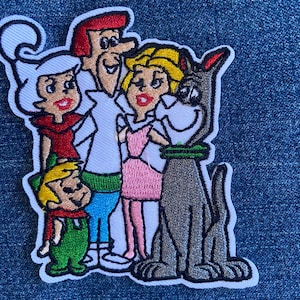 May include: Embroidered patch featuring the cartoon family, The Jetsons, and their dog, Astro. The patch shows the family in their signature outfits, with vibrant colors and a white border. The patch is on a denim background.