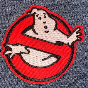 May include: A red and black embroidered patch with a white ghost in the center. The ghost has a surprised expression and is surrounded by a red circle with a black outline. The text "No Ghost" is written in black letters across the circle.
