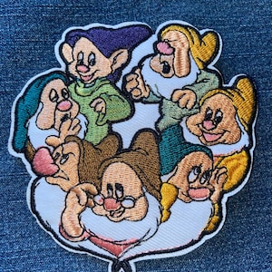 May include: Embroidered patch featuring the seven dwarfs from Snow White. The patch has a white border and depicts the dwarfs in various colors, including green, purple, yellow, and brown. The patch is likely for clothing or accessories.